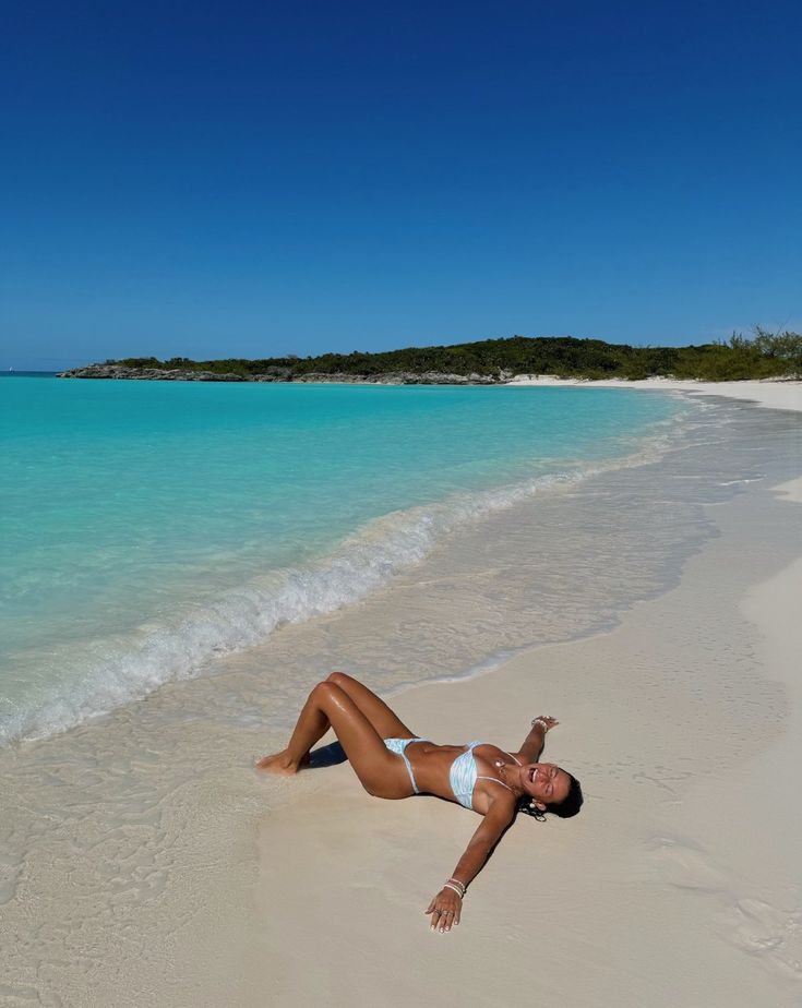 Woman lying on the sand beside turquoise water on a sunny beach.