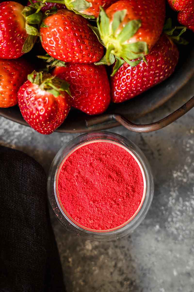 Fresh strawberries beside a bowl of red strawberry powder.