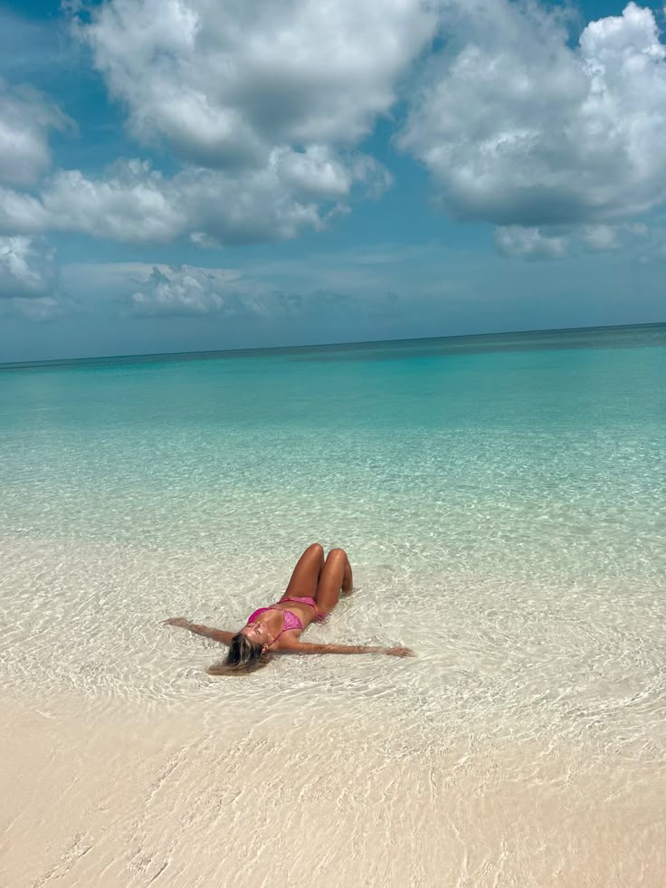 Woman relaxing in shallow turquoise seawater beneath a cloudy sky.