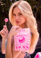 Woman holding a pink lollipop and packaging outdoors with blonde hair. The lollipops are peptide collagen peptide lollipops with vitamins. The Healthiest Lollipops In The World!
