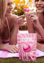 Two women enjoying pink lollipops with a product packaging in the foreground. Woman enjoying It Girl Vitamins collagen peptide lollipop beauty supplement