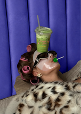 Woman wearing sunglasses and hair rollers with a green lollipop and an iced drink balanced on her head.