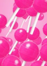 Close-up of glossy pink It Girl peptide lollipops with white sticks arranged against a pink background.